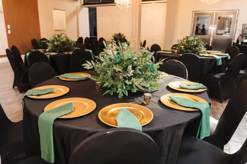 A table set with gold chargers, dark linen and green floral runners