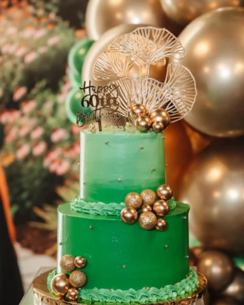 A tiered green and gold celebration cake surrounded by balloons