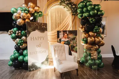 A gold and green balloon arch behind a decorated celebration chair