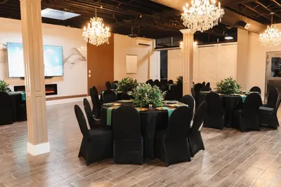 A banquet room set with round tables, black linen and a chandelier