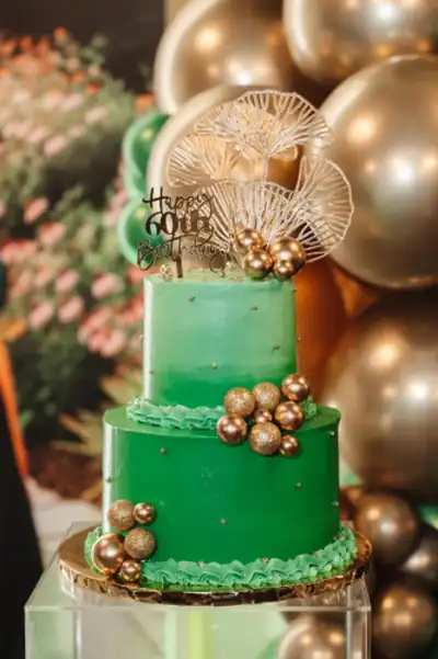 A tiered green and gold celebration cake surrounded by balloons