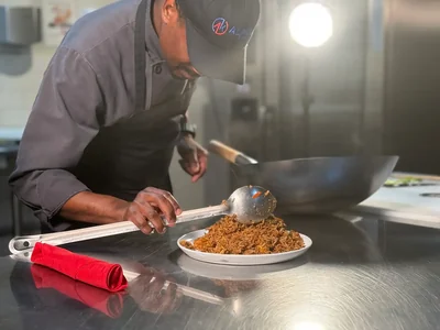 A chef spooning rice onto a plate in the kitchen