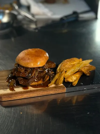 A grilled burger with fries and fried plantain on a wooden board