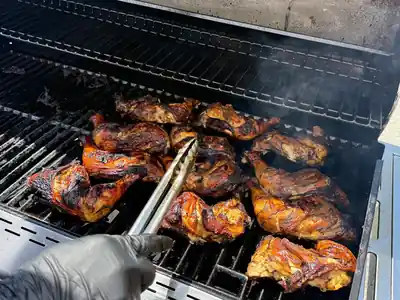 Jerk chicken quarters searing on a grill with tongs turning a piece